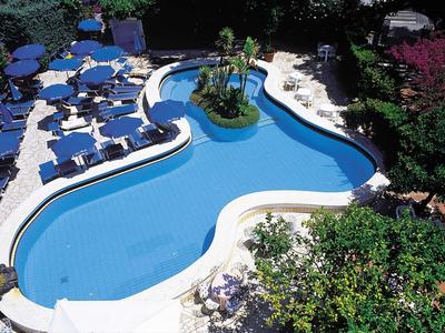 Piscine d'hôtel courbée avec chaises longues et végétation luxuriante autour.