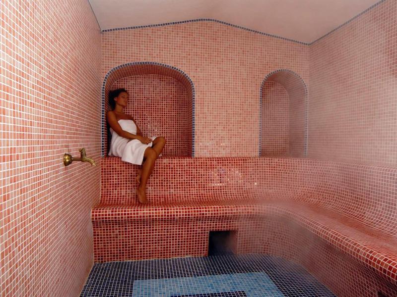 Femme se détend dans un hammam avec des carreaux roses et un sol bleu.