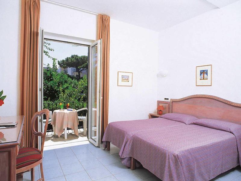 Chambre d'hôtel lumineuse avec deux lits et balcon donnant sur un feuillage vert