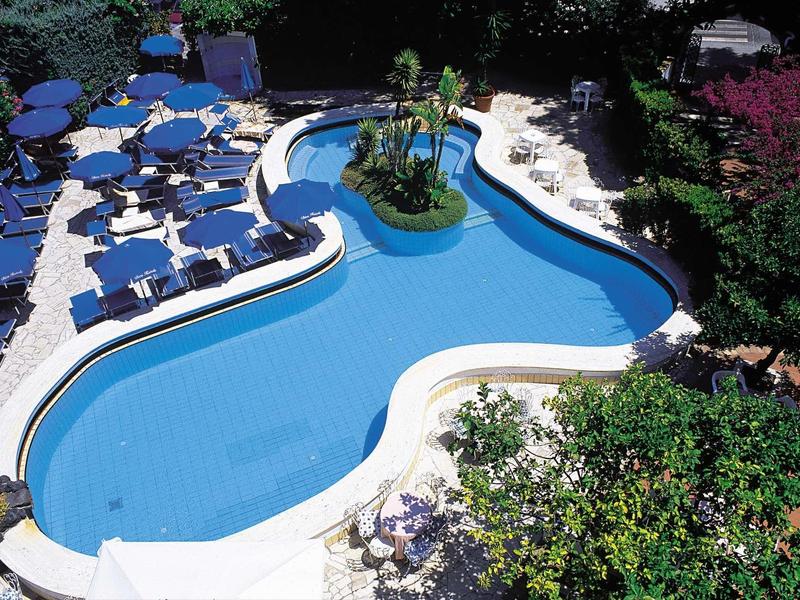Piscine d'hôtel courbée avec chaises longues et végétation luxuriante autour.
