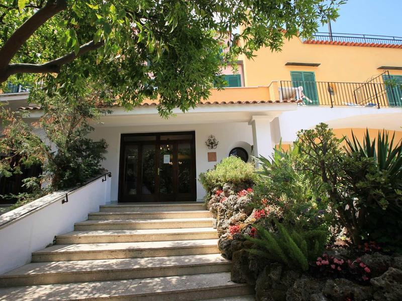 Entrée d'hôtel avec escaliers, plantes et lumière du soleil.