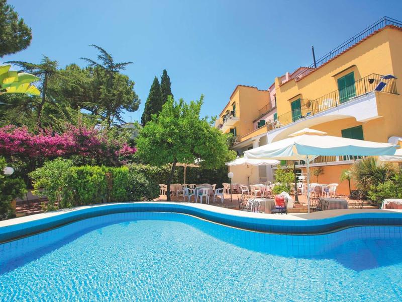 Hôtel avec piscine extérieure, parasols et fleurs colorées devant un bâtiment jaune.