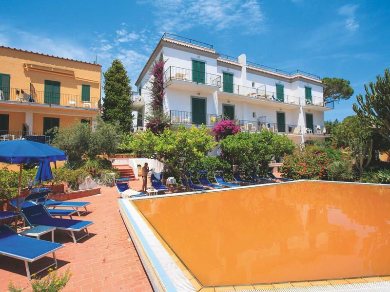 Bâtiments d'hôtel avec piscines vides et chaises longues sous un ciel bleu.