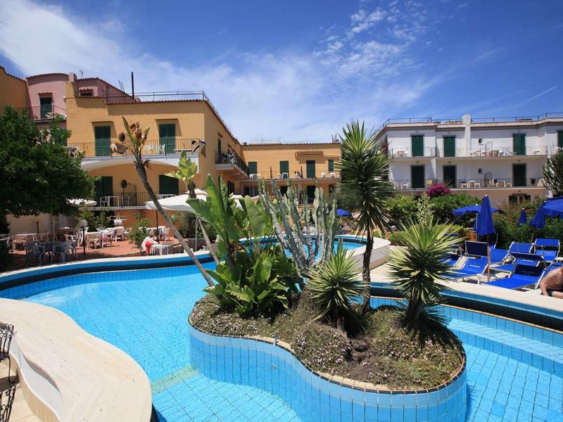 Piscine ronde d'hôtel avec îlot de plantes et transats sous un ciel ensoleillé.