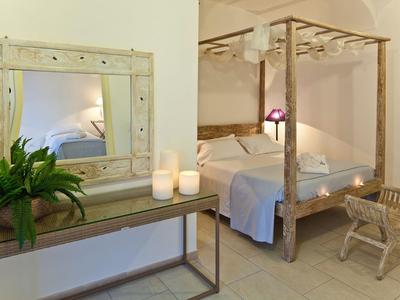 Przytulny pokój hotelowy z łóżkiem baldachimowym, drewnianym lustrem, świecami i zieloną rośliną.