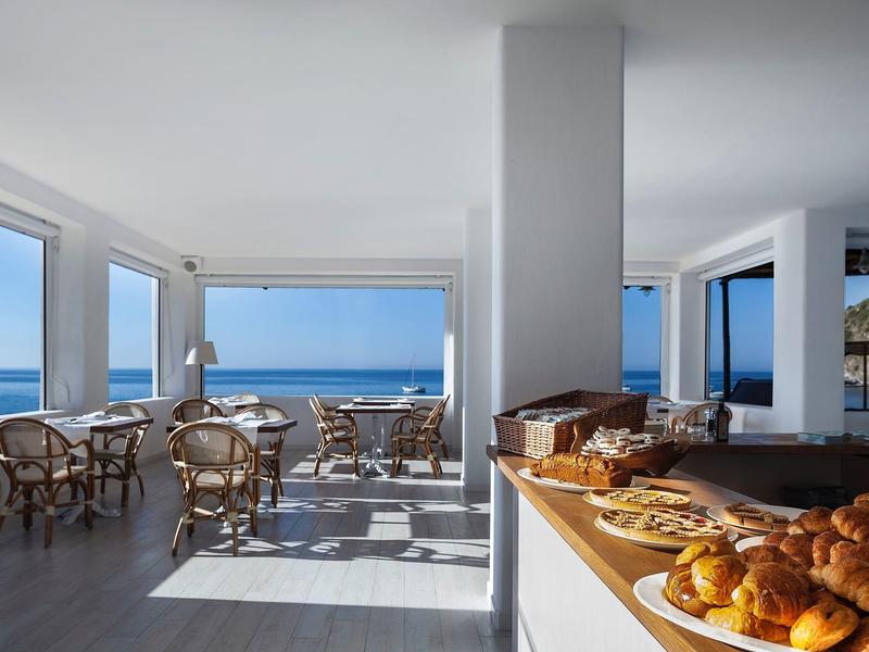 Moderner Frühstücksraum mit Panoramafenstern, gedeckten Tischen und Buffet mit Backwaren am Meer.