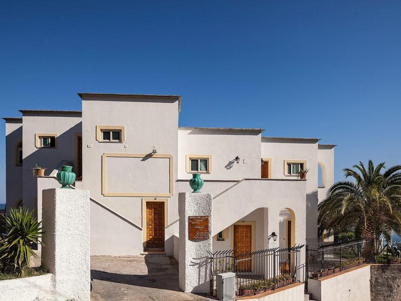 Modernes, weißes Haus mit rechteckigen Fenstern und Holzterrassen vor klarem blauem Himmel.