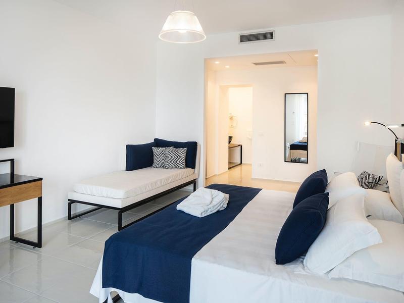 Helles Schlafzimmer mit großem Bett, Einzelbett, blau-weißer Bettwäsche und minimalistischem Mobiliar.