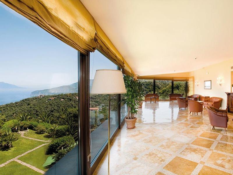 Große Terrasse mit Fliesenboden, Blick auf das Meer und grüne Hügel, helle Lounge-Möbel.