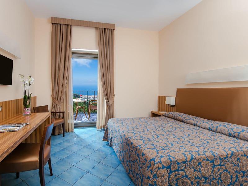 Modernes Hotelzimmer mit Doppelbett, Schreibtisch und Meerblick durch die Balkontür.