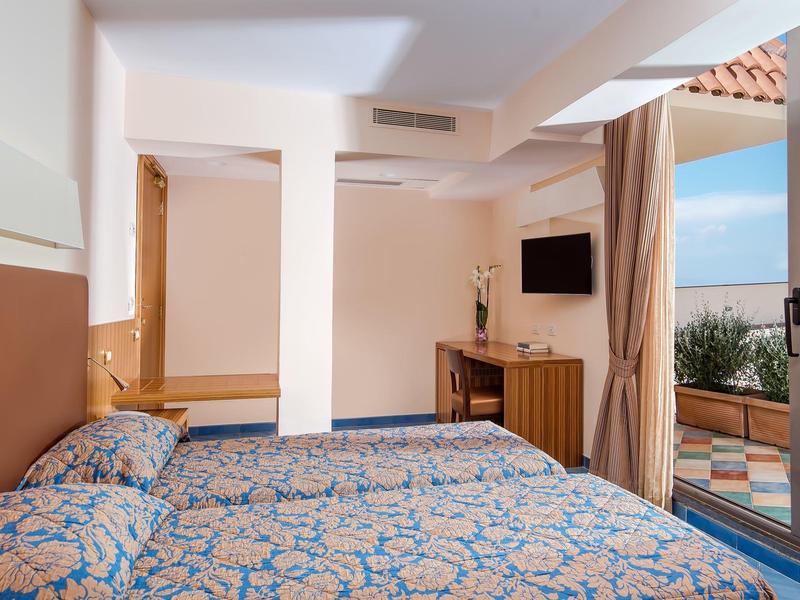 Hotelzimmer mit zwei Betten, Fernseher und Blick auf die Terrasse mit Meerblick