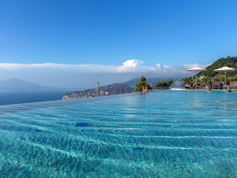 Infinity-Pool mit klarem Wasser und Blick auf das Meer und die Berge bei Sonnenschein.