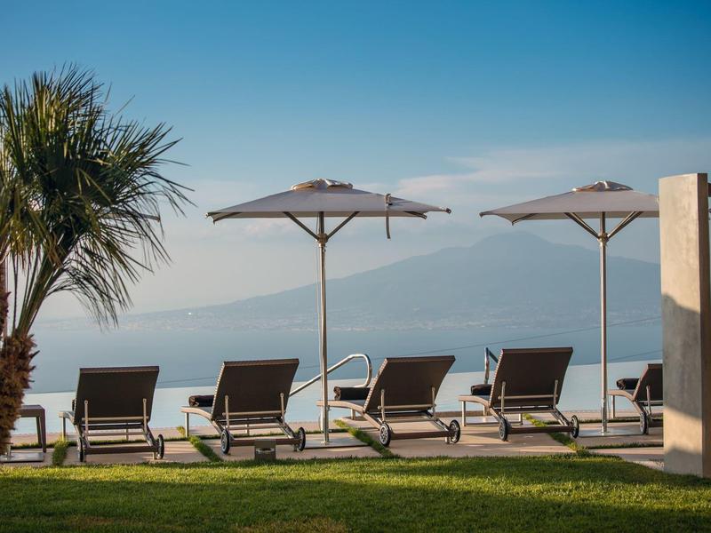 Poolliegen und Sonnenschirme neben einem Infinity-Pool mit Blick auf das Meer bei klarem Wetter.