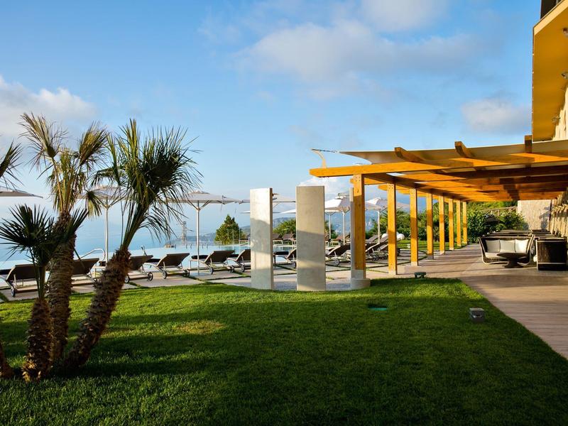 Hotelterrasse mit Holzdach, modernen Sitzgelegenheiten und Blick auf das Meer bei sonnigem Wetter.