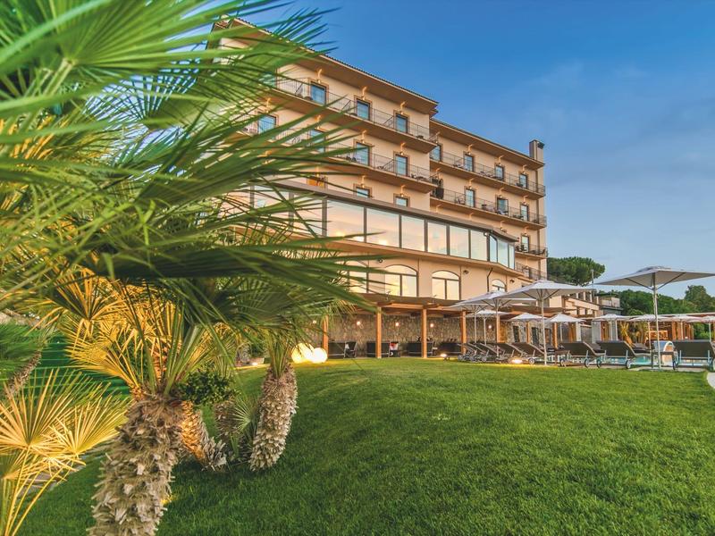 Hotelgebäude mit Balkon und Liegestühlen sowie Palmen im Vordergrund bei blauem Himmel.