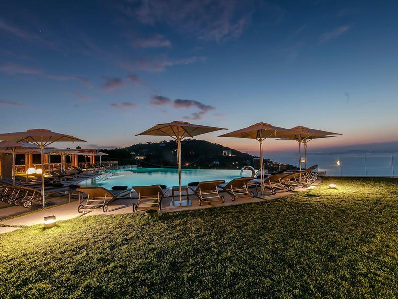 Abendliche Poollandschaft mit Liegestühlen und Sonnenschirmen nahe dem Meer in einem Hotelresort.