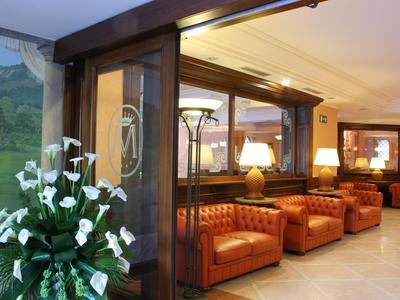 Heller Hotellobby mit braunen Ledersesseln und Blumendekoration am Eingang.