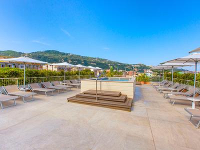Dachterrasse mit Liegestühlen und Sonnenschirmen, umgeben von Bergen und klarem Himmel.
