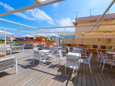 Dachterrasse mit weißen Stühlen und Tischen, umgeben von Gebäuden und Bergen im Hintergrund.