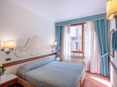 Helles Hotelzimmer mit Doppelbett, blauer Bettdecke und großem Fenster mit blauen Vorhängen.