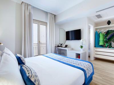 Helles Hotelzimmer mit großem Bett, Fernseher und Kleiderschrank mit Kleidung.