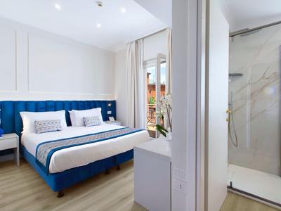 Modernes Hotelzimmer mit blauem Doppelbett, Holzboden und angrenzendem Badezimmer mit Dusche.