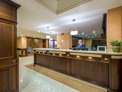 Rezeption mit dunklem Holz in einem Hotel, beleuchtet und gepflegt, Mitarbeiter am Tresen.