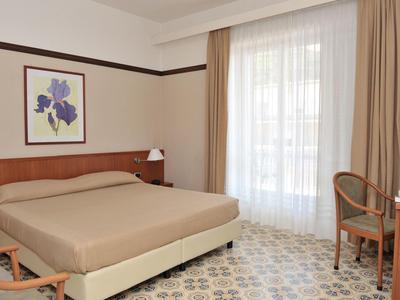 Modern hotelkamer met tweepersoonsbed, bureau, stoelen en raam met gordijnen.