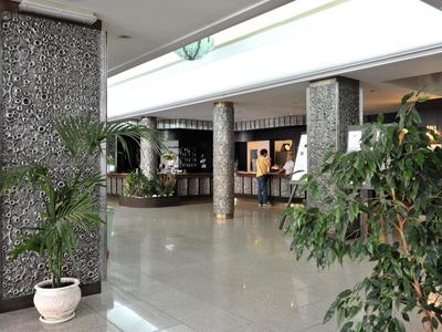 Ruime hotelhal met planten, marmeren vloer en receptie op de achtergrond.