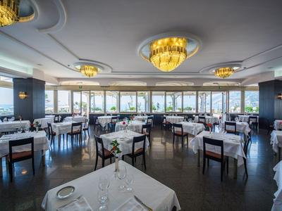 Elegant restaurant met wit gedekte tafels en grote ramen met uitzicht op de haven.