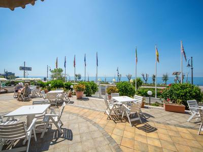 Außerhalb eines Hotels mit Sitzbereichen, Sonnenschirmen und Blick aufs Meer.
