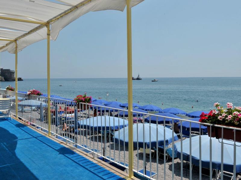 Balkon met witte tafels en blauwe stoelen met uitzicht op zee bij heldere lucht.
