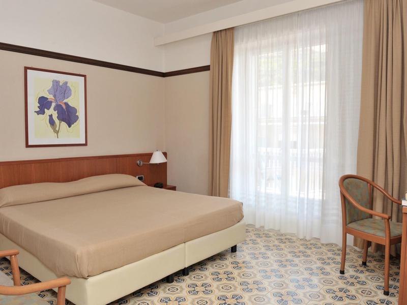 Modern hotelkamer met tweepersoonsbed, bureau, stoelen en raam met gordijnen.