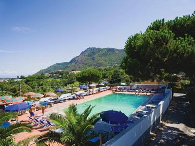Blick auf einen Poolbereich mit blauen Sonnenschirmen und Liegestühlen vor einer grünen Berglandschaft.