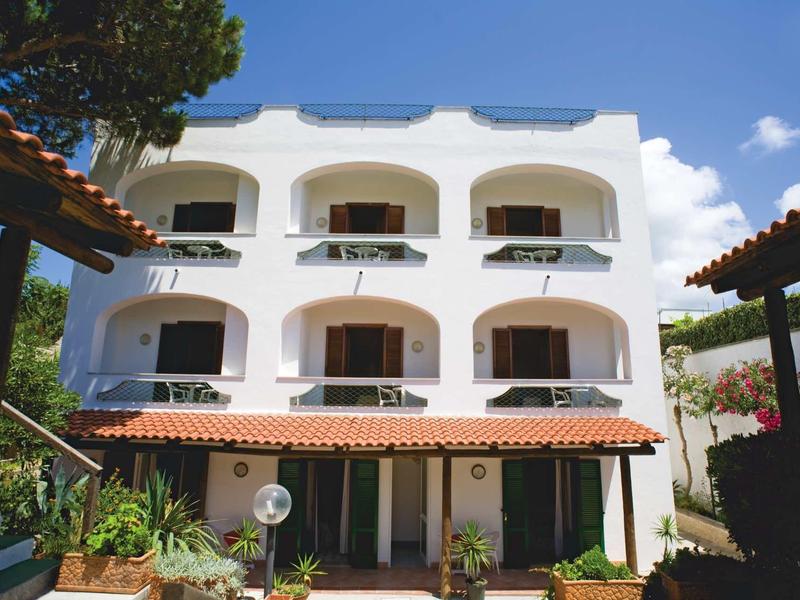 Weißes dreistöckiges Gebäude mit Bögen, Balkon und Pflanzen unter blauem Himmel.