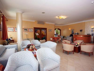 Großer Aufenthaltsraum mit weißen Sesseln, beige Wänden, Kunstwerken und Holzmöbeln.