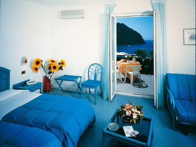 Helles Zimmer mit blauer Einrichtung, Sonnenblumen, offenem Balkon und Meerblick.