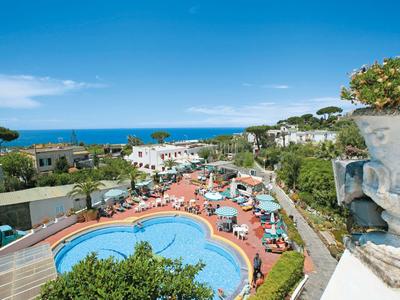 Hotelpool mit Sonnenschirmen und Liegen, Blick aufs Meer unter blauem Himmel.