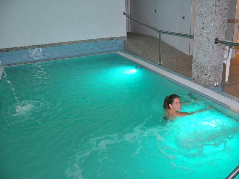 Donna rilassata in piscina interna illuminata con fontana e ringhiera in vetro.