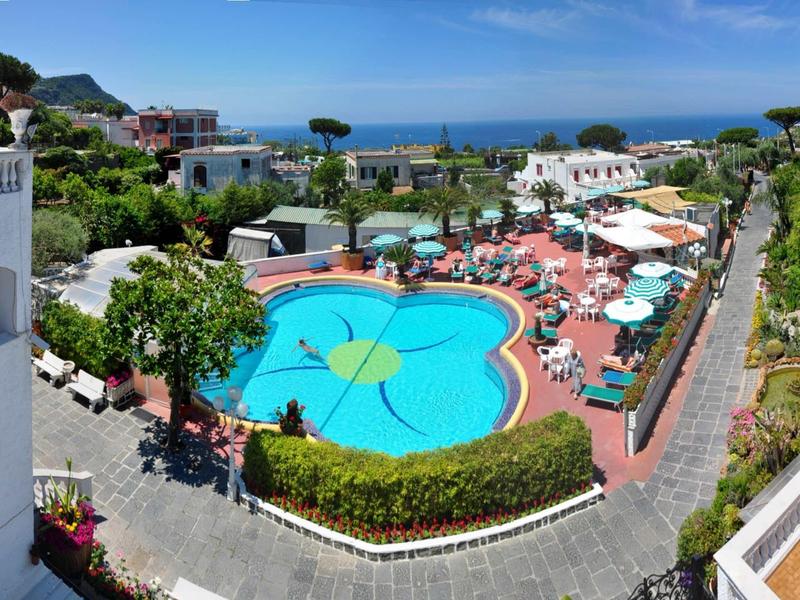 Piscina dell'hotel con bordo rotondo e sagomato, circondata da lettini e vista mare sullo sfondo.