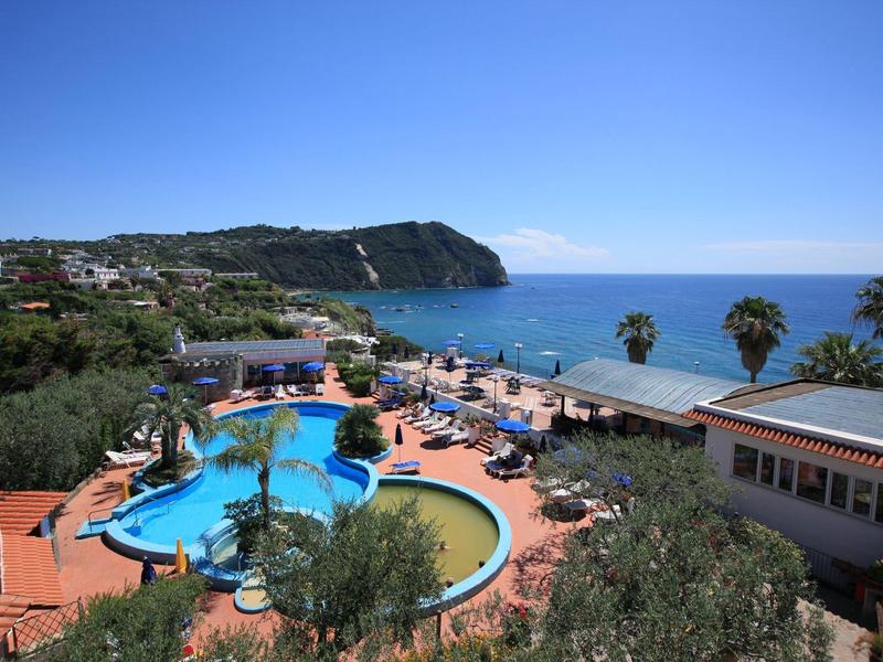 Hotel met buitenzwembad, ligstoelen en uitzicht op zee en kustklif bij helder weer