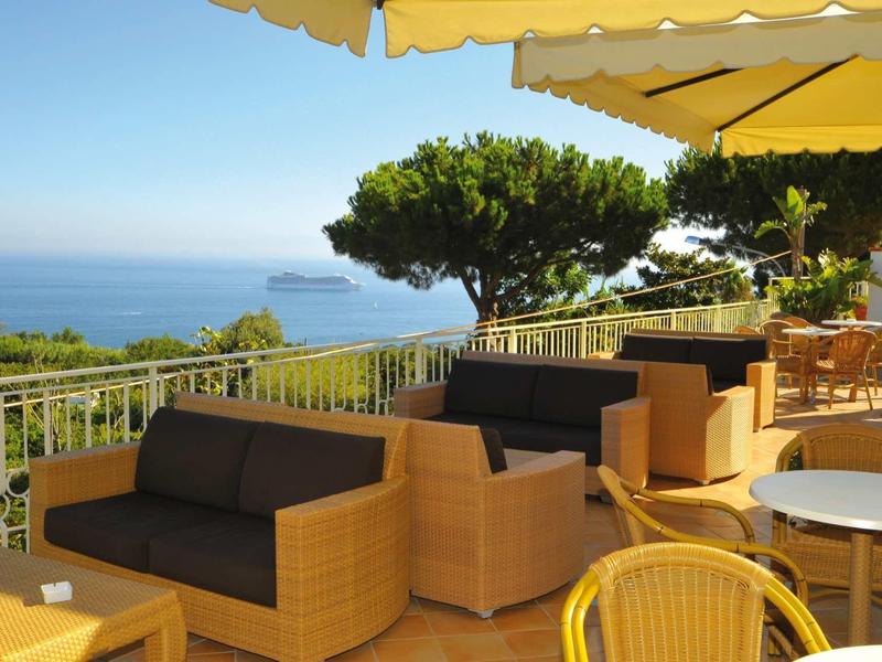Terrace with seating areas under umbrellas overlooking the sea and an island.
