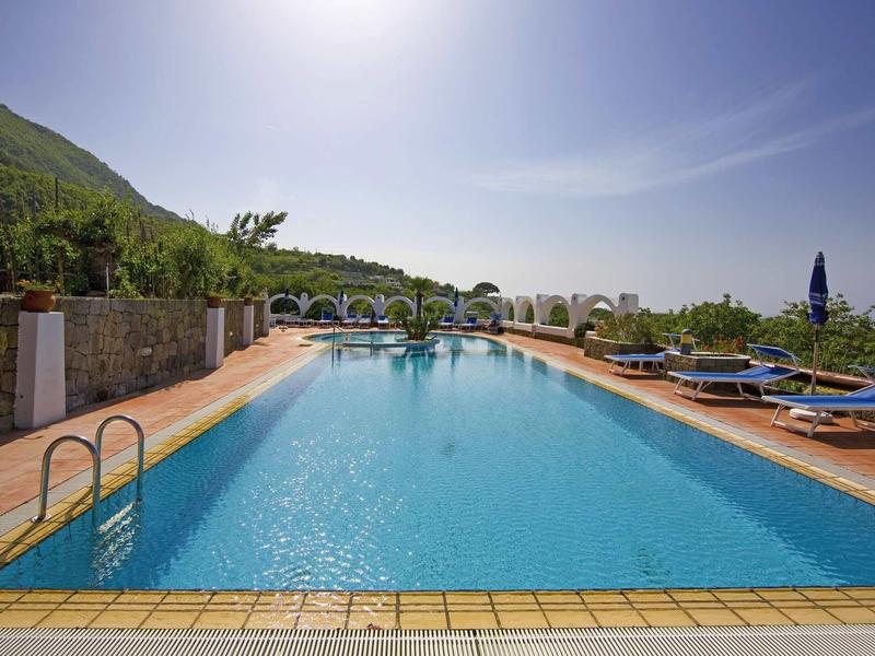 Outdoor pool with lounge chairs and umbrellas under clear skies and mountain view.