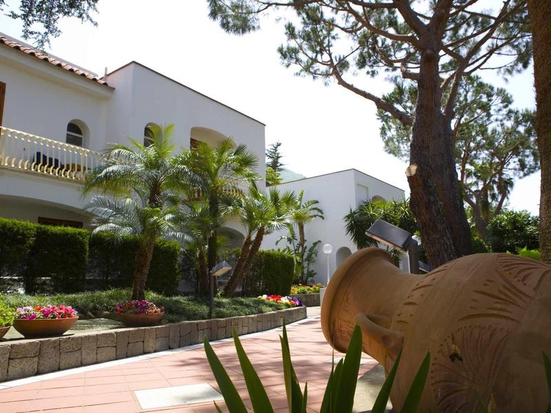 Hotel courtyard with white facade, plants, and decorative pottery.