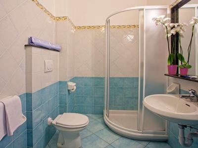 Kleines Badezimmer mit runder Dusche, Toilette, Waschbecken und blauen Fliesen an den Wänden.