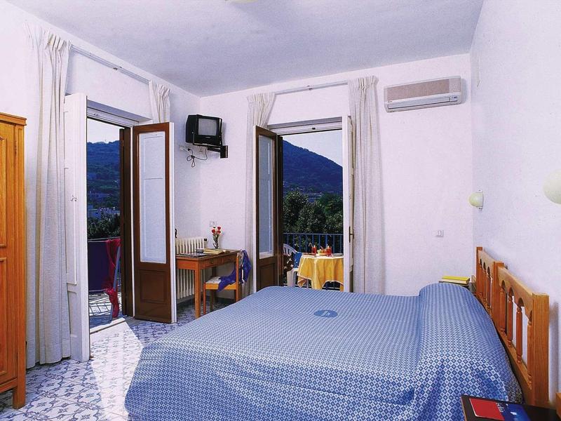 Hell eingerichtetes Schlafzimmer mit Doppelbett, offenem Balkon und Bergblick.