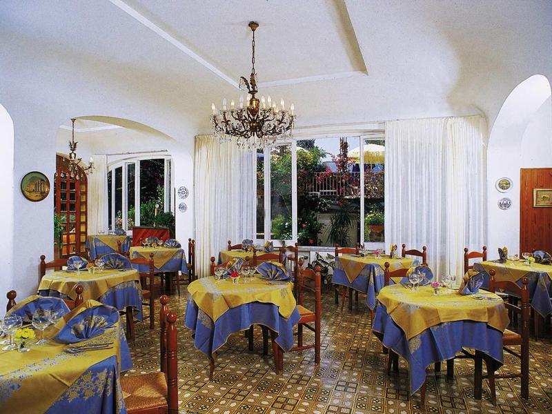 Gemütlicher Essraum mit blau-gelb gedeckten Tischen, Kronleuchter und großen Fenstern.