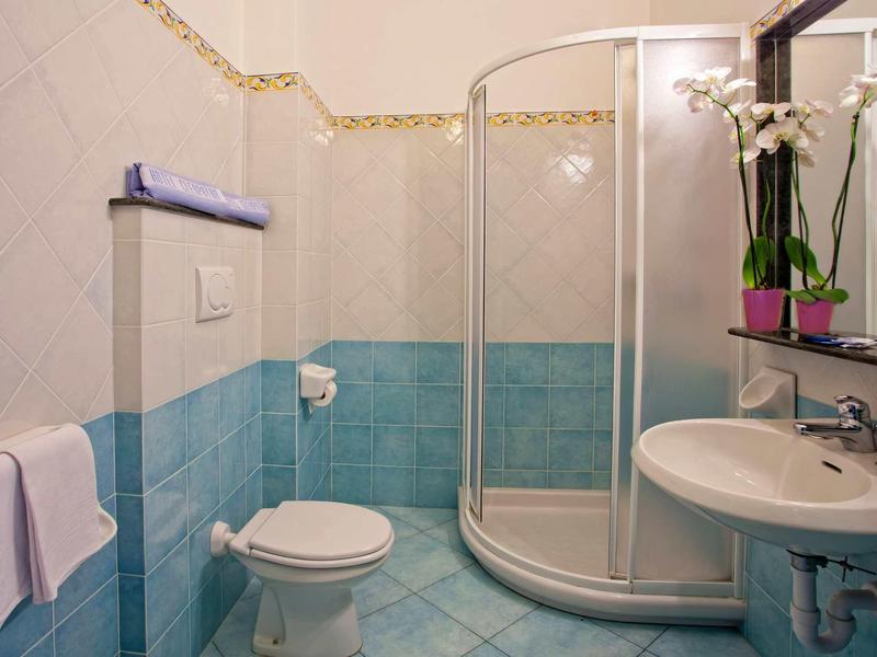 Kleines Badezimmer mit runder Dusche, Toilette, Waschbecken und blauen Fliesen an den Wänden.