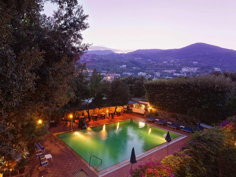 Beleuchteter Pool mit Sitzplätzen und Hügeln im Hintergrund bei Dämmerung.