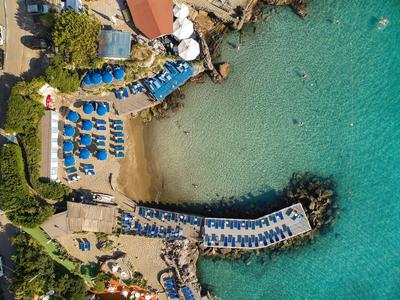 Letecký pohled na pláž s modrými slunečníky a průzračnou vodou vedle hotelu.